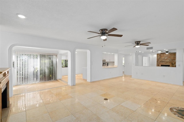 unfurnished living room featuring ceiling fan, a textured ceiling, and a large fireplace