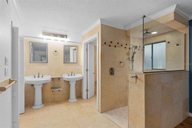 bathroom with a textured ceiling, crown molding, tiled shower, and tile walls