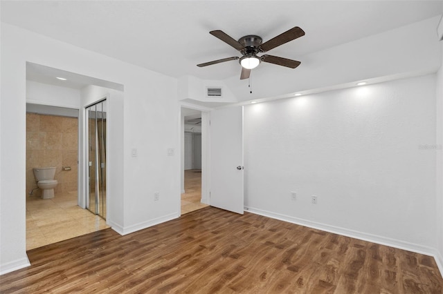 unfurnished bedroom featuring ceiling fan, dark wood-type flooring, ensuite bathroom, and a closet