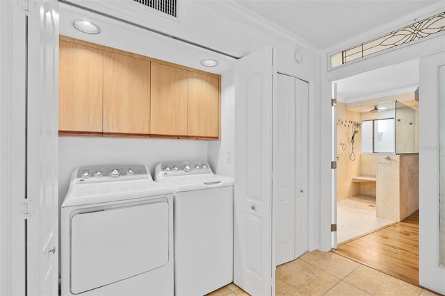 washroom featuring crown molding, washing machine and dryer, light hardwood / wood-style flooring, and cabinets