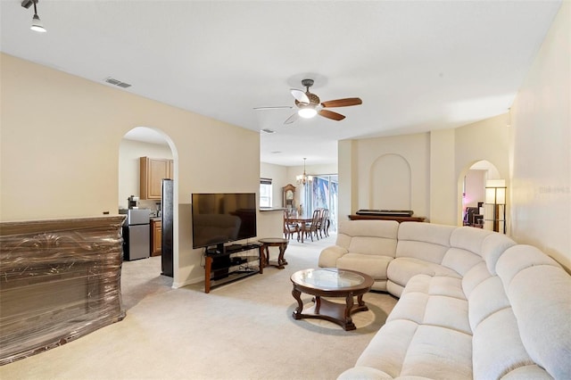 carpeted living room with ceiling fan with notable chandelier