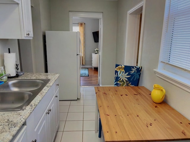 kitchen with light stone counters, white cabinets, light tile patterned floors, sink, and white appliances