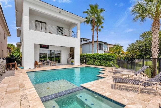 back of property with a balcony, a swimming pool with hot tub, and a patio area