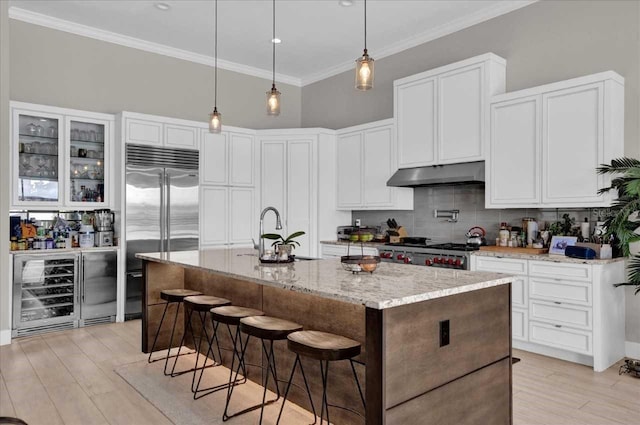 kitchen with light stone counters, beverage cooler, a center island with sink, appliances with stainless steel finishes, and light wood-type flooring