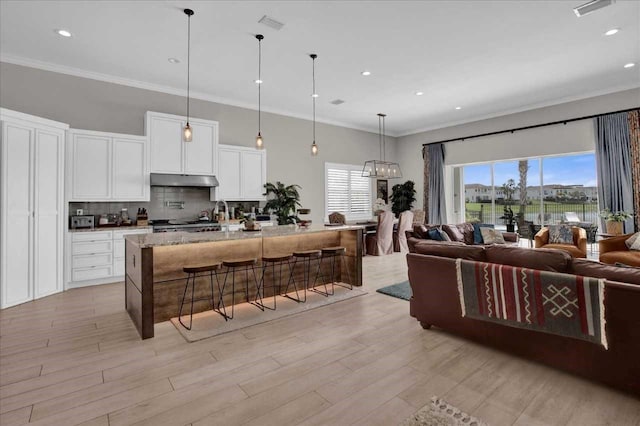 kitchen with light hardwood / wood-style floors, white cabinetry, a center island with sink, decorative light fixtures, and light stone countertops