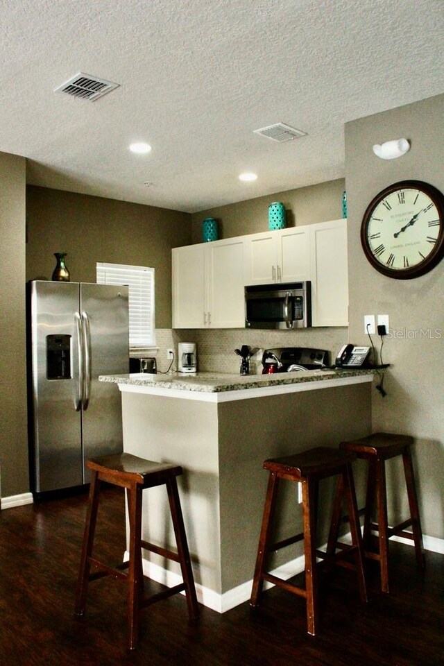 kitchen with stainless steel appliances, dark wood-type flooring, white cabinetry, and a breakfast bar