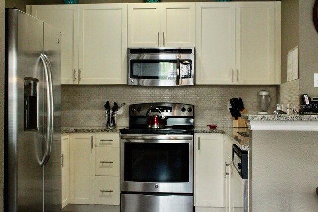 kitchen with light stone counters, white cabinets, stainless steel appliances, and decorative backsplash