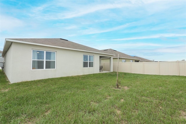 rear view of property with stucco siding, fence, a yard, and a shingled roof
