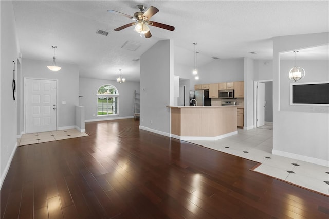 unfurnished living room featuring ceiling fan with notable chandelier, lofted ceiling, a textured ceiling, and light hardwood / wood-style flooring