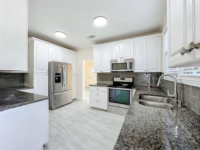 kitchen featuring white cabinets, visible vents, dark stone counters, stainless steel appliances, and a sink