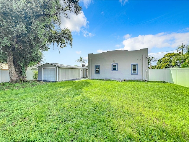 rear view of house featuring fence, a garage, stucco siding, an outbuilding, and a yard