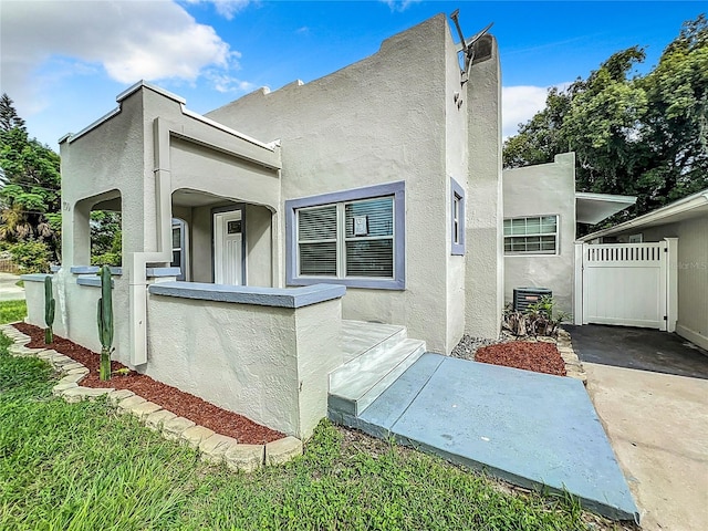 view of front facade with a gate, stucco siding, fence, and central air condition unit