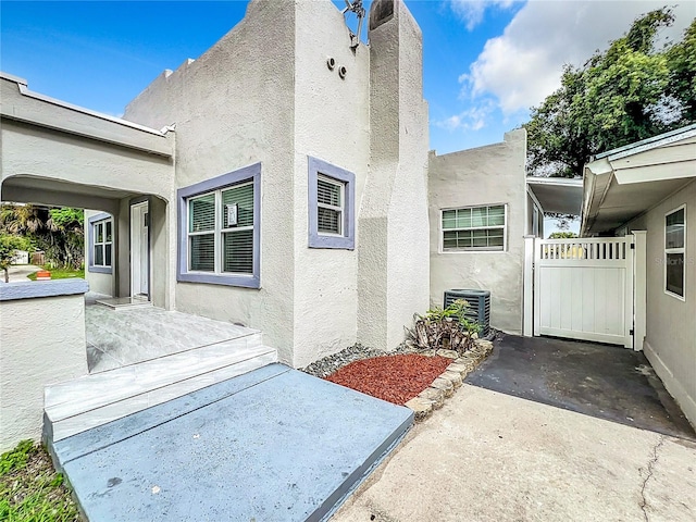 exterior space featuring stucco siding, a gate, central AC unit, and a patio