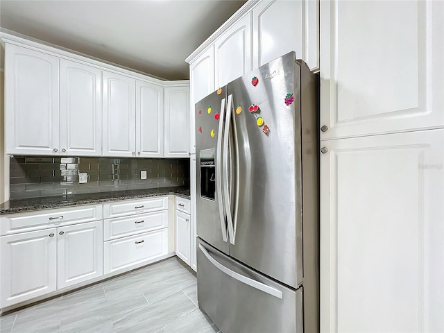 kitchen with decorative backsplash, white cabinets, dark stone counters, and stainless steel fridge