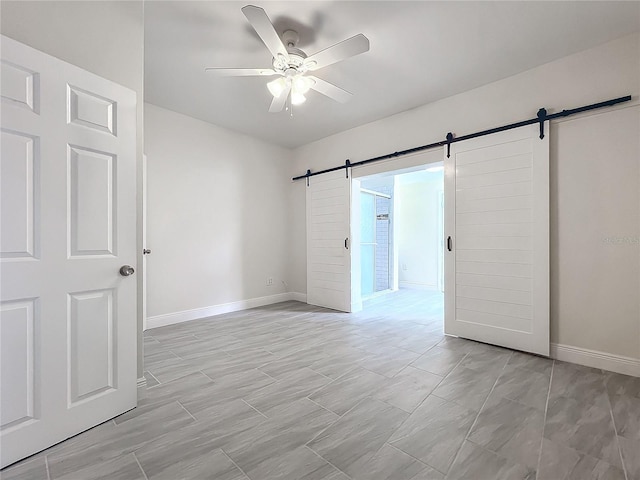 unfurnished room with a ceiling fan, baseboards, and a barn door