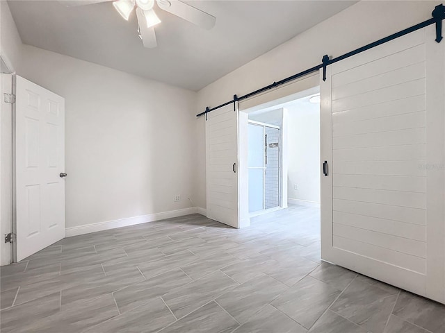 unfurnished room with a ceiling fan, baseboards, and a barn door