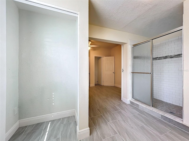 bathroom with a textured ceiling, baseboards, ceiling fan, and a shower stall