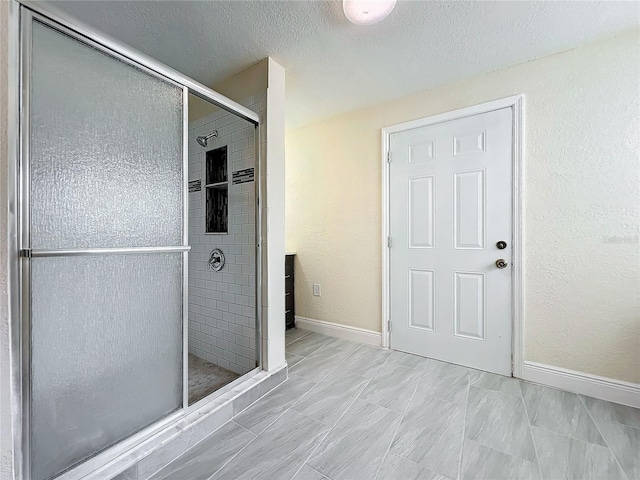 bathroom with baseboards, a textured ceiling, a textured wall, and a shower stall