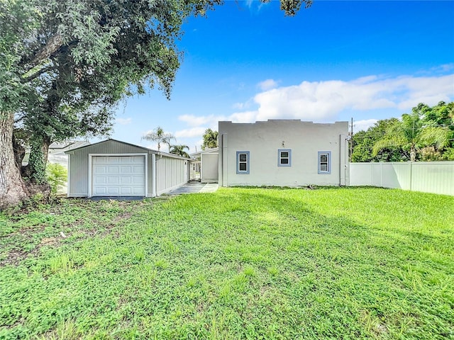 rear view of house with fence, a garage, stucco siding, an outbuilding, and a yard