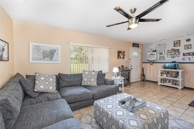 living room featuring light tile patterned floors, wooden walls, and ceiling fan