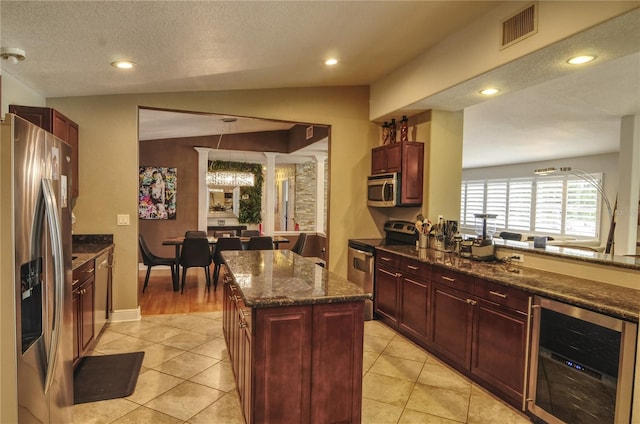 kitchen featuring appliances with stainless steel finishes, vaulted ceiling, a kitchen island, a textured ceiling, and beverage cooler