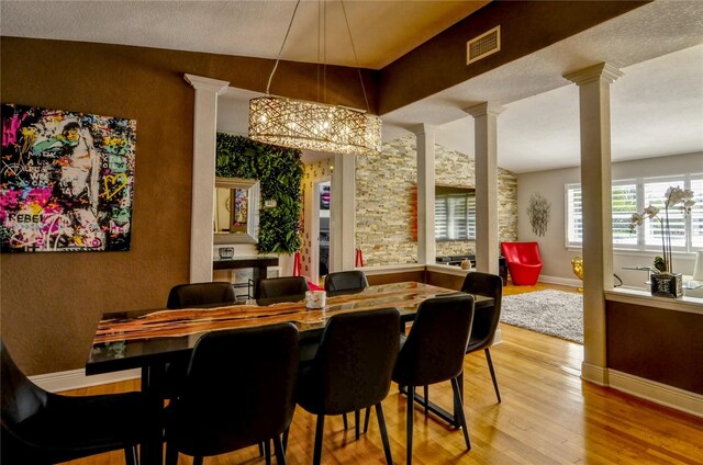 dining area with a textured ceiling, hardwood / wood-style flooring, a notable chandelier, vaulted ceiling, and decorative columns