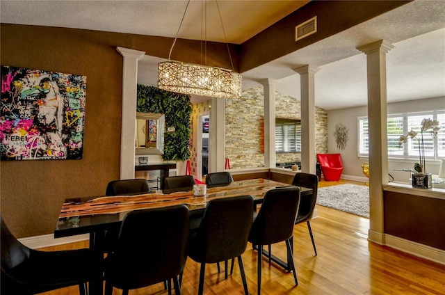 dining room with visible vents, baseboards, a chandelier, wood finished floors, and ornate columns