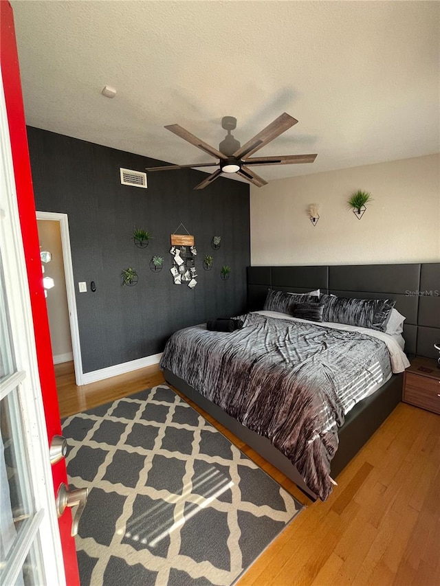 bedroom with visible vents, a ceiling fan, a textured ceiling, wood finished floors, and baseboards