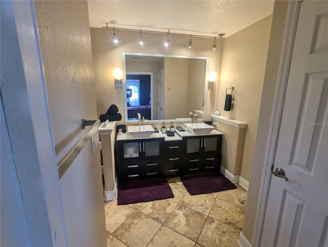 bathroom featuring track lighting, double vanity, baseboards, and tile patterned floors