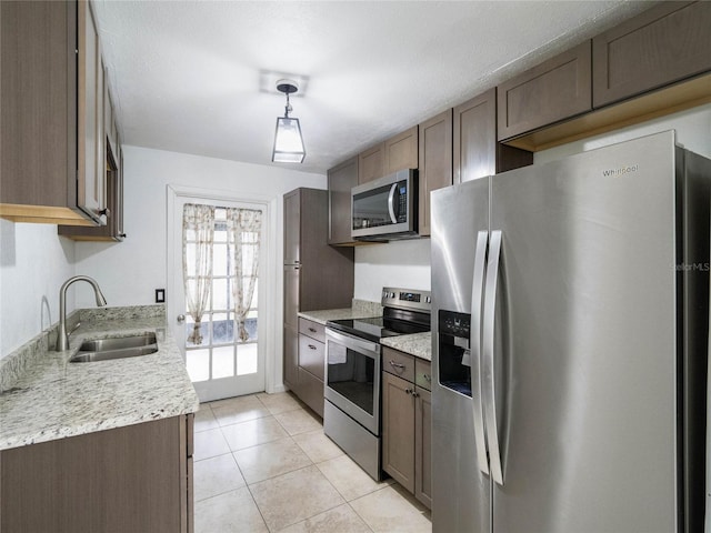 kitchen with appliances with stainless steel finishes, light stone counters, light tile patterned floors, decorative light fixtures, and sink