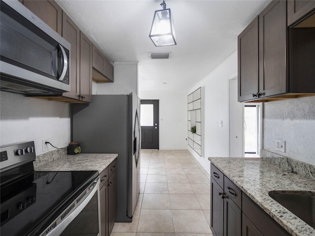 kitchen featuring dark brown cabinetry, light stone countertops, light tile patterned flooring, and appliances with stainless steel finishes