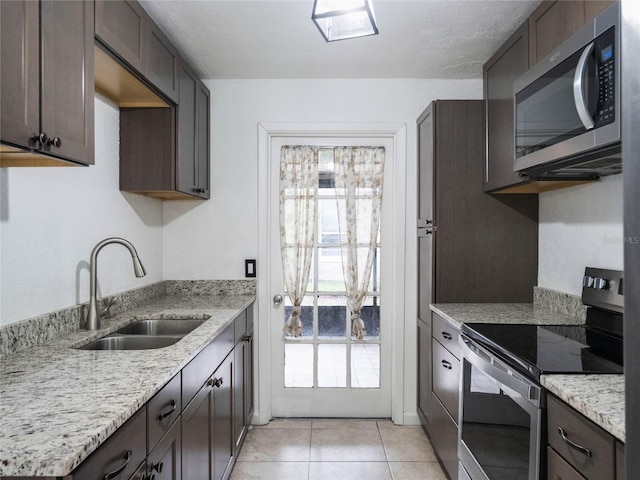 kitchen featuring light tile patterned flooring, sink, stainless steel appliances, and light stone counters