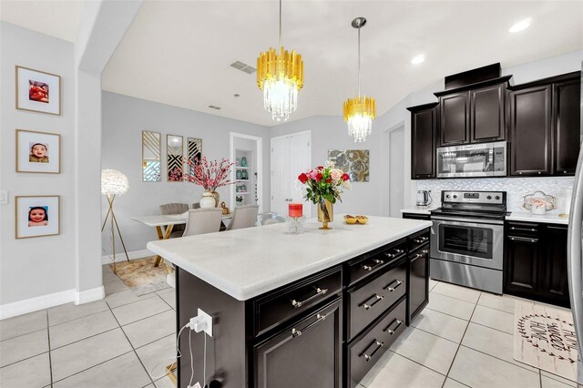 kitchen with light tile patterned flooring, hanging light fixtures, a kitchen island, appliances with stainless steel finishes, and an inviting chandelier