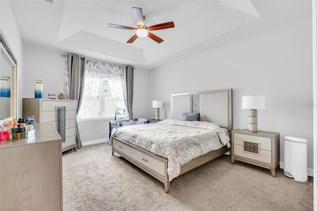 bedroom featuring a raised ceiling, ceiling fan, and light carpet