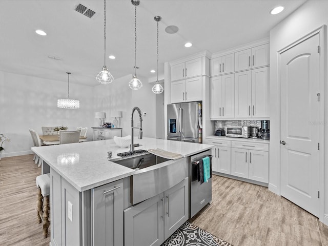 kitchen featuring appliances with stainless steel finishes, light wood-type flooring, pendant lighting, a breakfast bar area, and a center island with sink