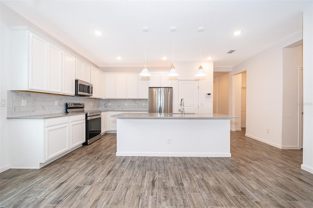 kitchen with appliances with stainless steel finishes, a kitchen island with sink, light hardwood / wood-style flooring, white cabinetry, and hanging light fixtures