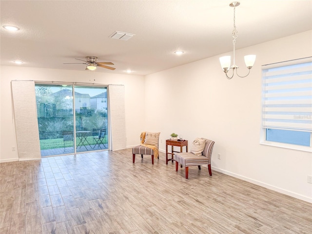 living area featuring ceiling fan with notable chandelier and light hardwood / wood-style floors