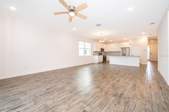 unfurnished living room featuring ceiling fan with notable chandelier