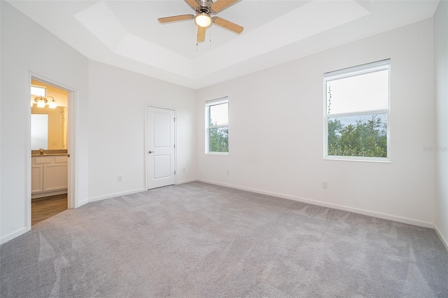 unfurnished bedroom featuring ensuite bathroom, a raised ceiling, ceiling fan, and light colored carpet