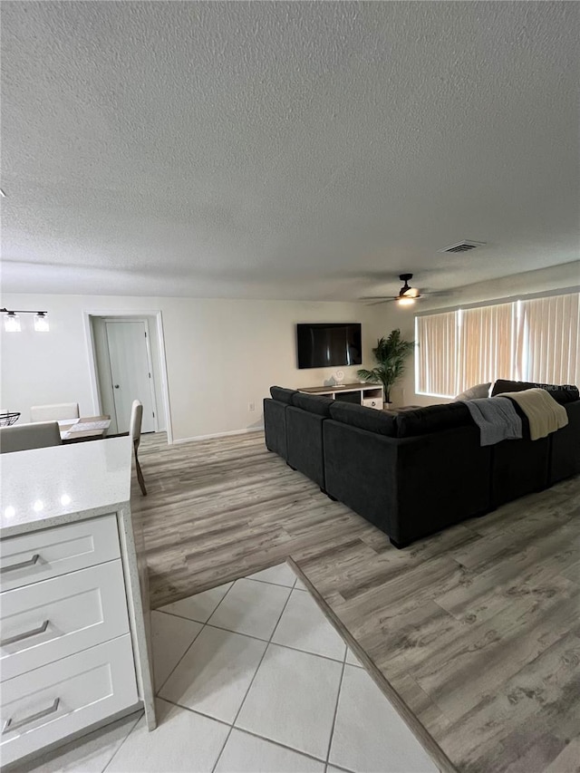 living room with ceiling fan, a textured ceiling, and light hardwood / wood-style floors