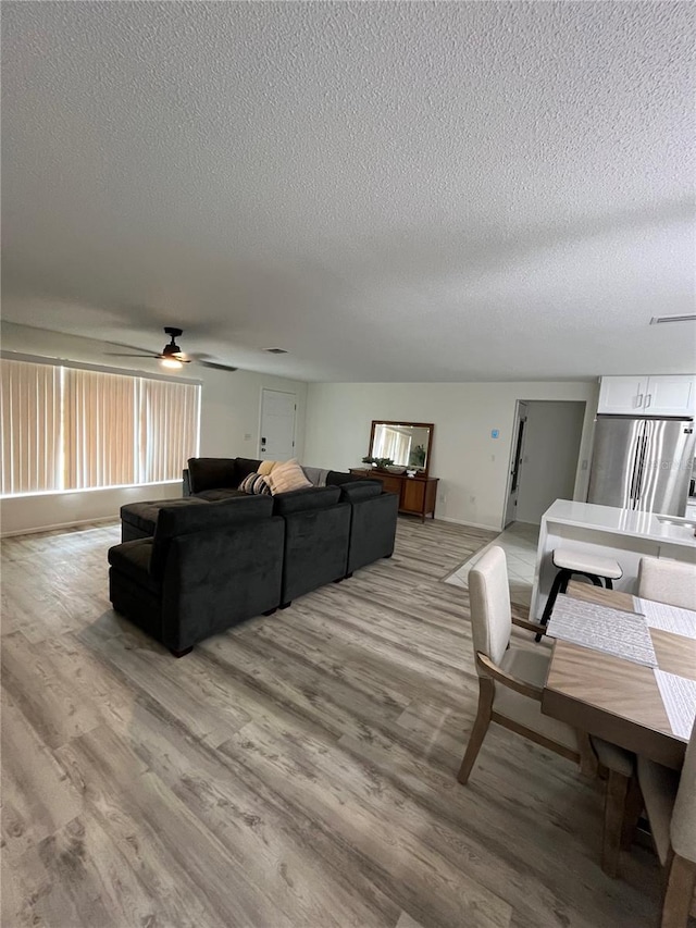 living room with ceiling fan, a textured ceiling, and light hardwood / wood-style floors