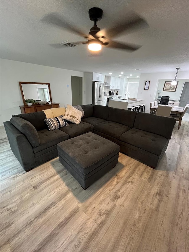 living room with ceiling fan, a textured ceiling, light hardwood / wood-style flooring, and sink