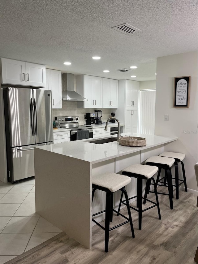 kitchen featuring wall chimney exhaust hood, a kitchen bar, white cabinetry, and appliances with stainless steel finishes