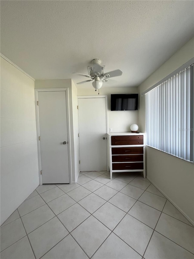 unfurnished bedroom with a textured ceiling, light tile patterned floors, and ceiling fan