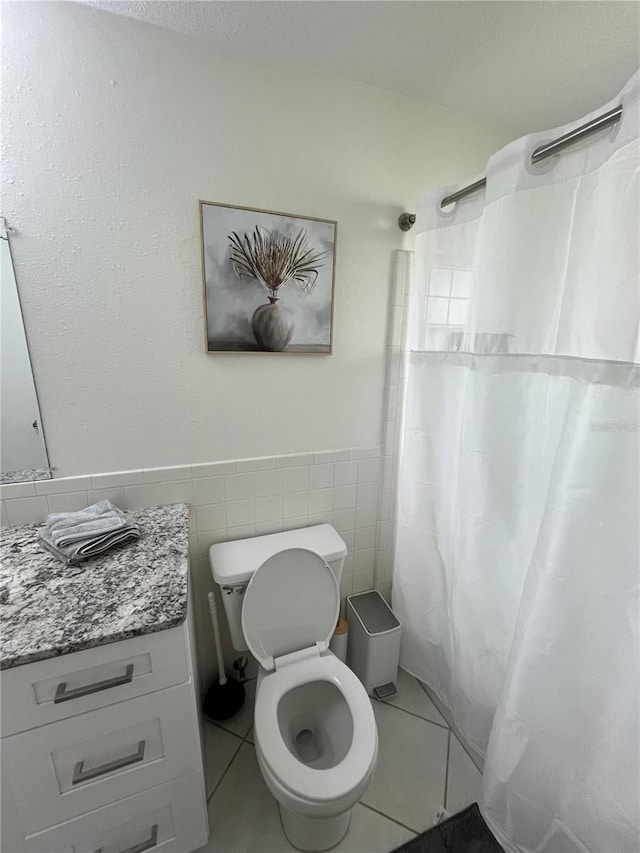 bathroom with vanity, toilet, walk in shower, tile walls, and tile patterned flooring