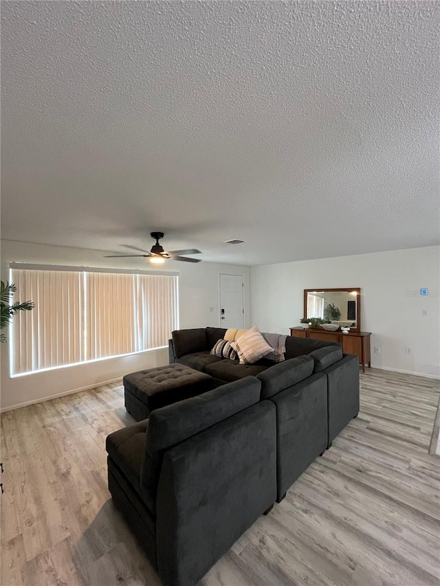 living room with a healthy amount of sunlight, light hardwood / wood-style floors, ceiling fan, and a textured ceiling