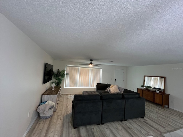 living room with light hardwood / wood-style floors, ceiling fan, and a textured ceiling