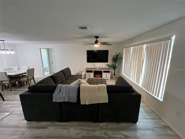 living room featuring light hardwood / wood-style floors, ceiling fan, and a textured ceiling