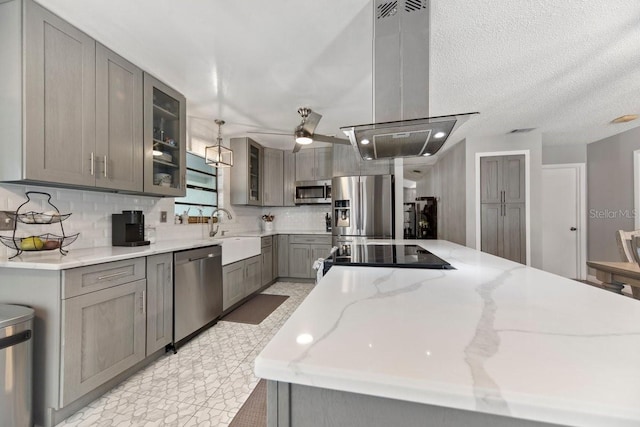 kitchen with light stone counters, island exhaust hood, gray cabinets, appliances with stainless steel finishes, and sink