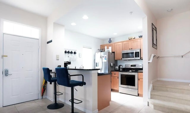 kitchen with a breakfast bar, light tile patterned floors, light brown cabinetry, appliances with stainless steel finishes, and kitchen peninsula